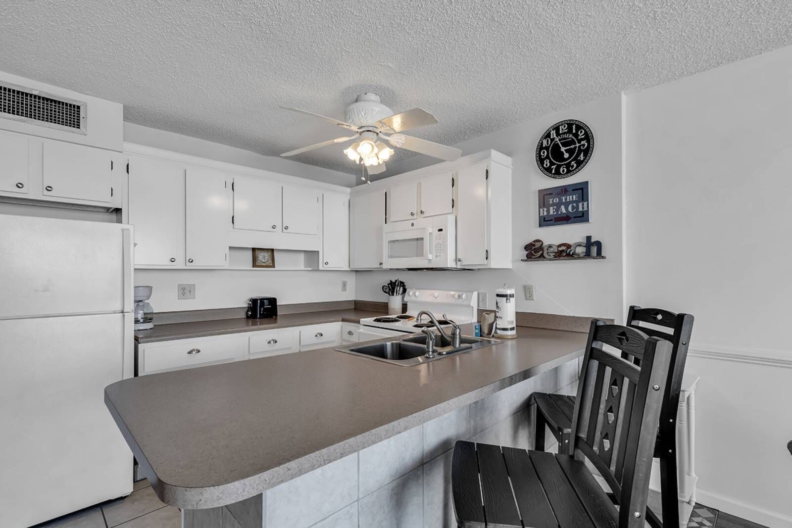 A modern kitchen with white cabinets, a central island, a ceiling fan, and a clock on the wall.