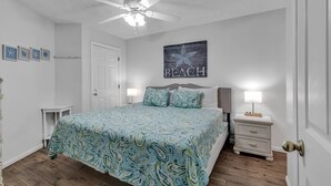 Ein Schlafzimmer mit einem Bett, zwei Nachttischen, einem Deckenventilator und einer Wand mit dem Schriftzug 'BEACH'.