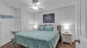A bedroom with a bed, two bedside tables, a ceiling fan, and a wall with a 'BEACH' sign.