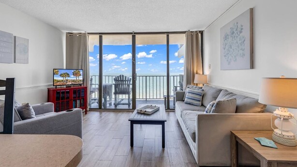 Ein geräumiges Wohnzimmer mit Balkon und Meerblick, einem Fernseher, einem roten Schrank und einer gemütlichen Sitzecke.