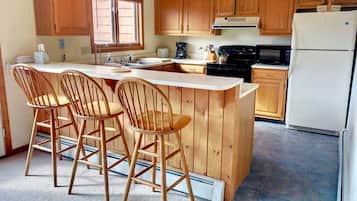 Una cocina con armarios de madera, una isla central con taburetes de bar, un refrigerador y un microondas.