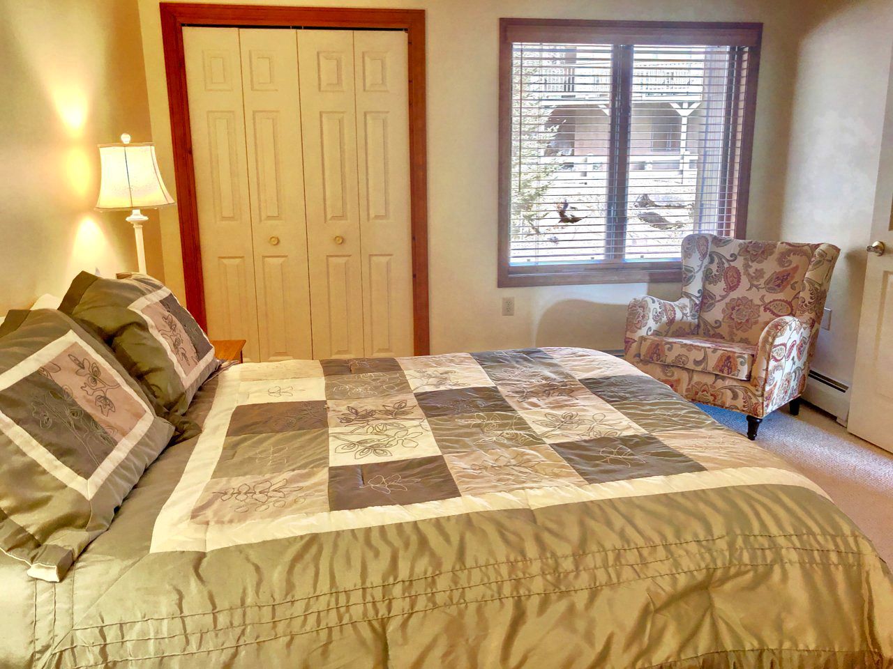 A bedroom with a bed, a chair, a lamp, a door, and a window.