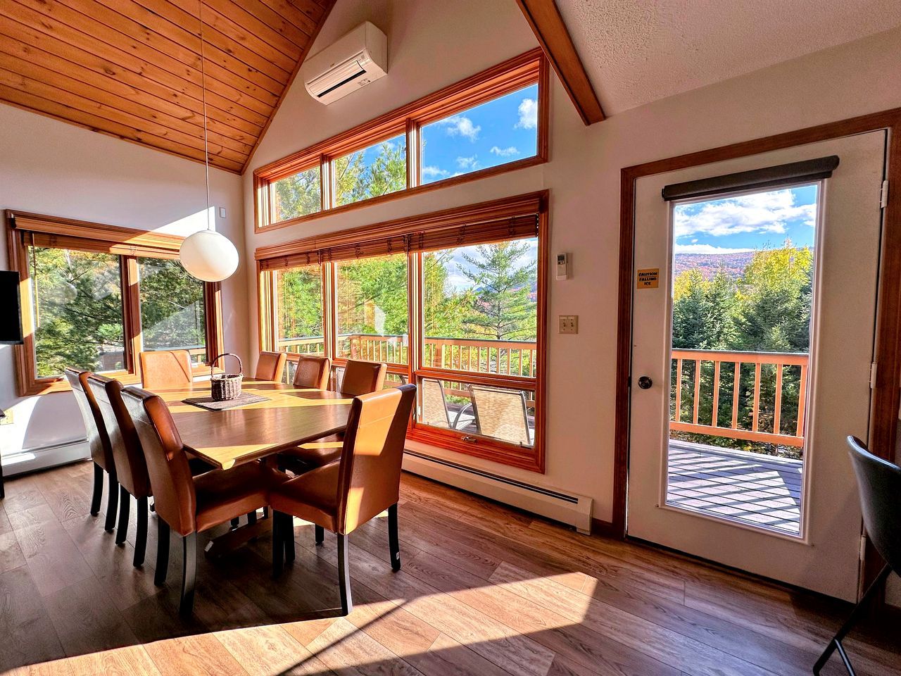 Un espace repas avec une table et des chaises en bois, de grandes fenêtres et une vue sur l’extérieur.