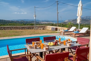 Ein Essbereich am Pool mit gedecktem Tisch für das Frühstück, mit Blick auf einen Pool und eine schöne Hügelkulisse.