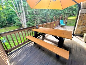 Eine Holzterrasse mit Picknicktischen und einem großen Sonnenschirm.