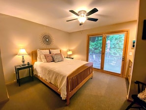Une chambre à coucher comprenant un lit, deux tables de chevet, un ventilateur de plafond et une vue sur l’extérieur grâce à une porte coulissante.