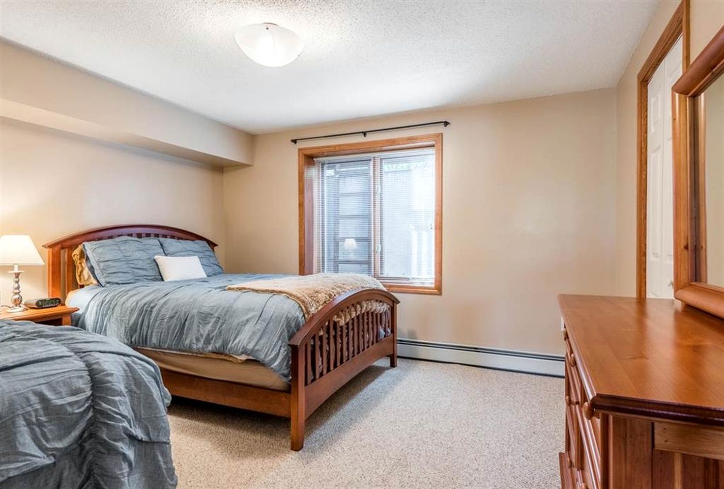 A bedroom with a bed, a nightstand, a dresser, and a window with blinds.