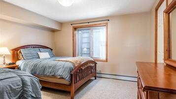 A bedroom with a bed, a nightstand, a dresser, and a window with blinds.