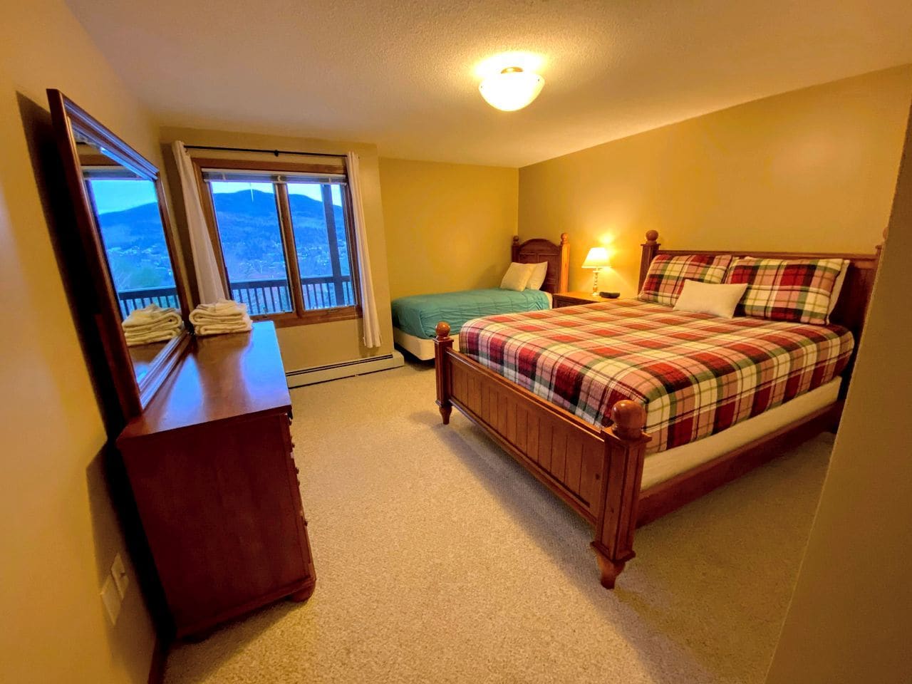 Une chambre à coucher avec un lit, une commode, une fenêtre donnant sur un beau paysage et un luminaire au plafond.