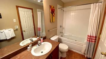 Une salle de bain avec deux lavabos, des toilettes, une baignoire et un rideau de douche.
