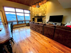 A spacious living area with a stone fireplace, a large window offering a mountain view, and a wooden dining table.
