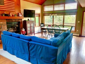 Ein Wohnzimmer mit Ecksofa, Kamin, Fernseher und einem Essbereich mit Stühlen und Tisch.