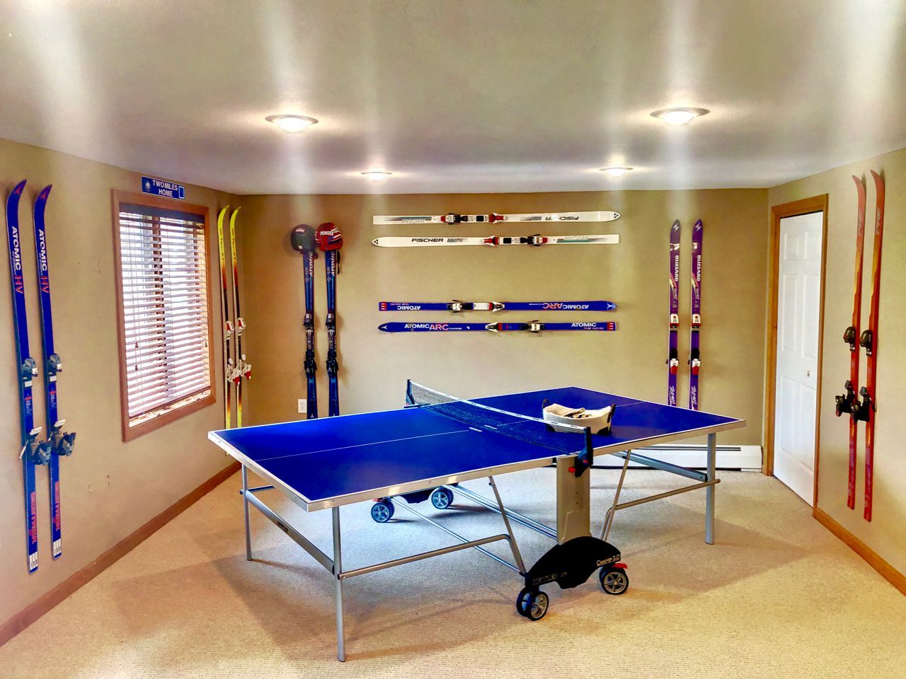 A room with two ping pong tables, skis, and a sign indicating 'WOMMELS HOME'.