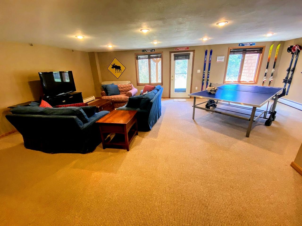 A room with a sofa, a table, a television, and a ping pong table.