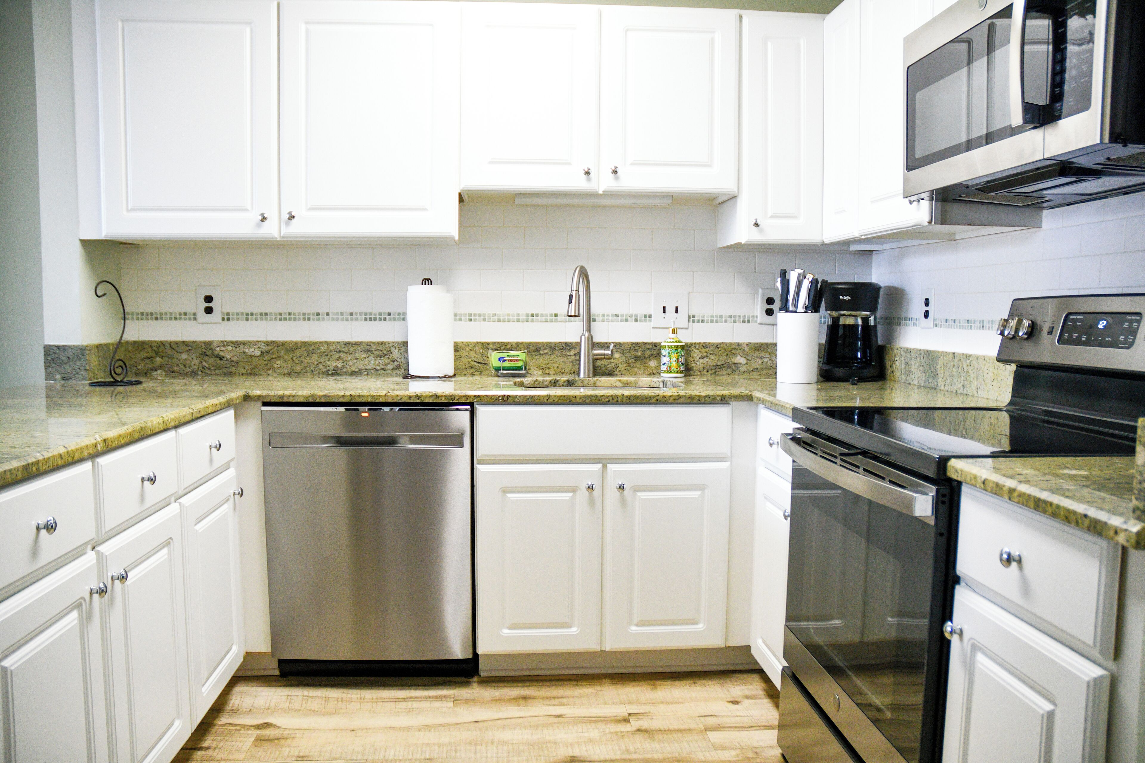A modern kitchen with white cabinets, stainless steel appliances, and a granite countertop.