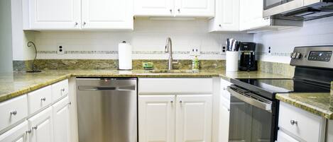 A modern kitchen with white cabinets, stainless steel appliances, and a granite countertop.