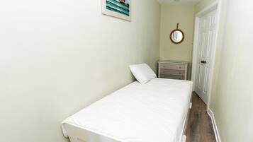 A narrow hallway leading to a bedroom with a bed, a dresser, a mirror, and a painting on the wall.