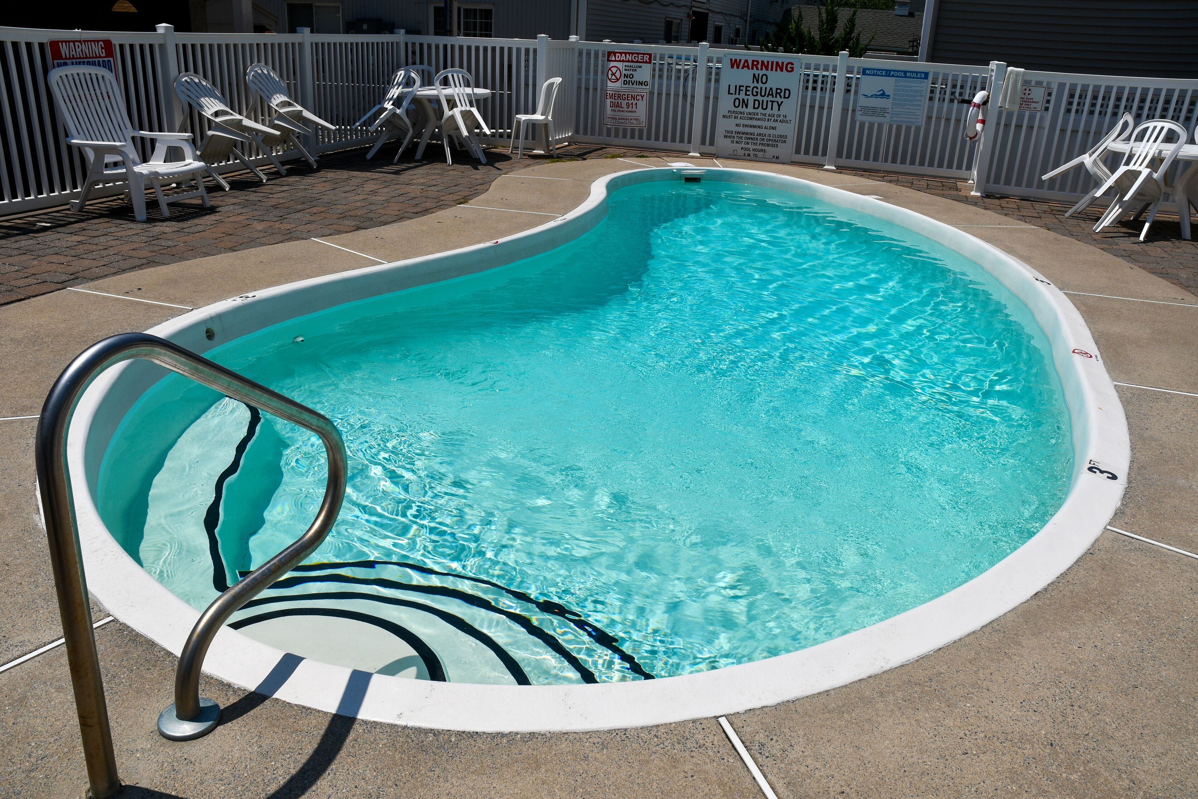 Una piscina con una escalera metálica, rodeada por una valla blanca y varias sillas de descanso.