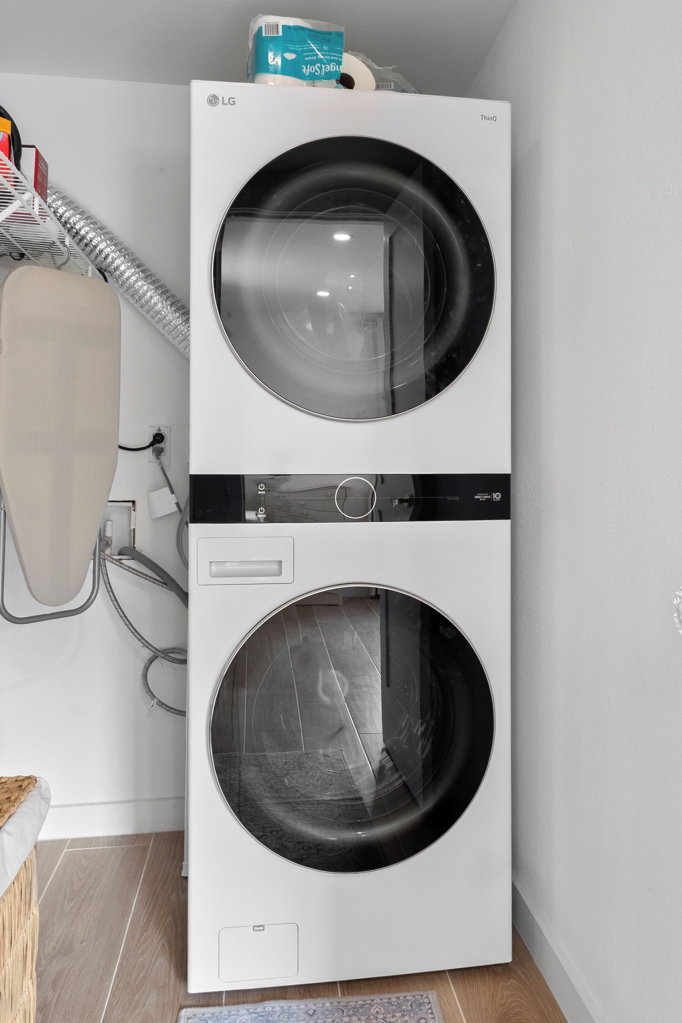 Een gestapelde wasmachine en droger met bedieningspaneel, een stroomkabel en een stofzuigerslang.