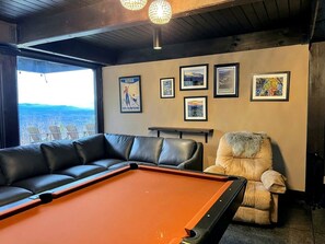 A billiards table with a pool cue, a black leather sofa, and a fur-covered armchair in a room with framed pictures on the wall. - Unique White Mountains Vacation Rental for Family Getaways in New England (Dalton)