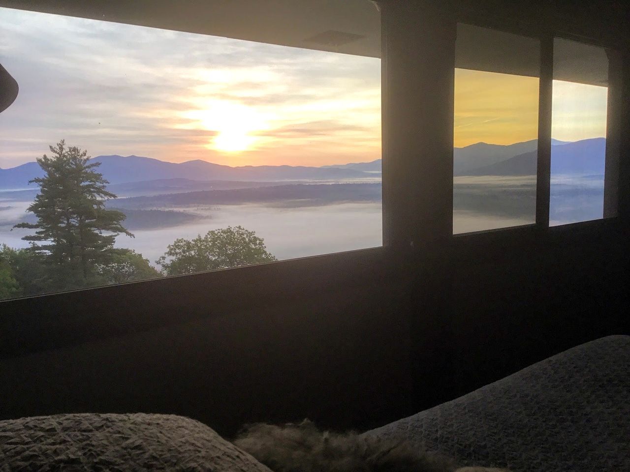 Une pièce dotée d’une grande fenêtre donnant sur un paysage montagneux au coucher du soleil.