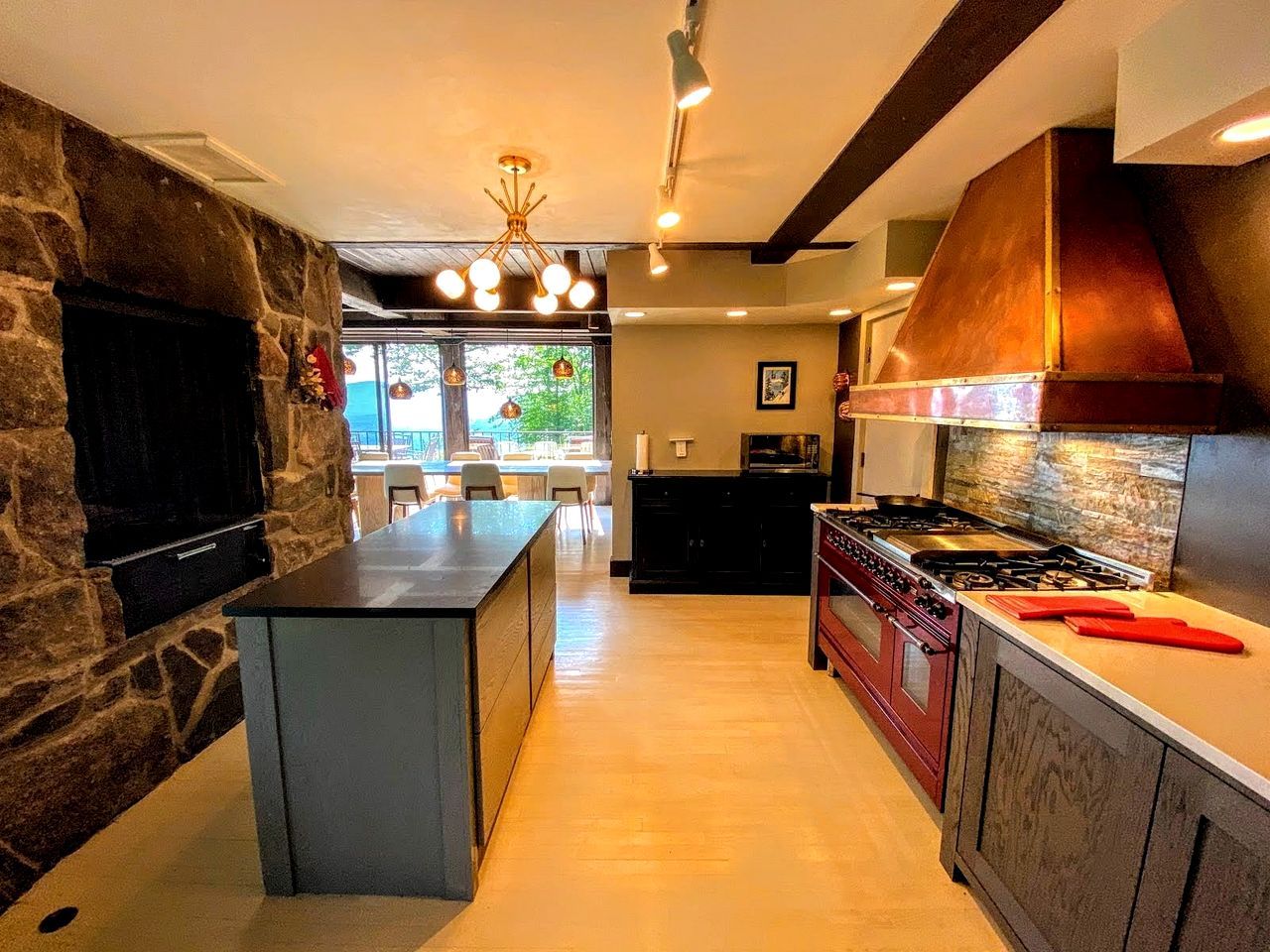 Une cuisine moderne dotée d’un îlot central, d’une cheminée en pierre et offrant une vue sur l’extérieur.
