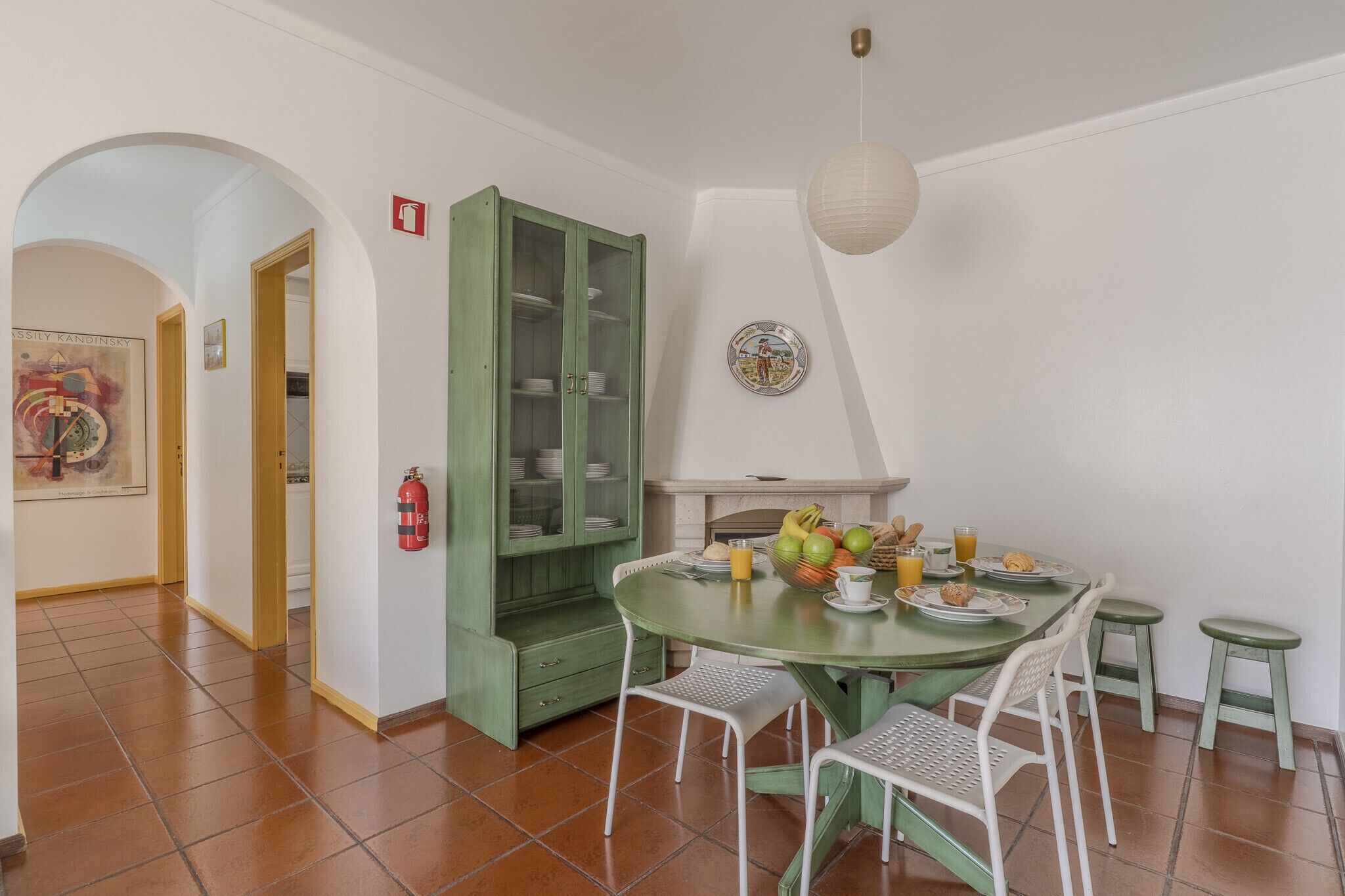 A dining area with a green table and chairs, a green cabinet, and a fire extinguisher on the wall.