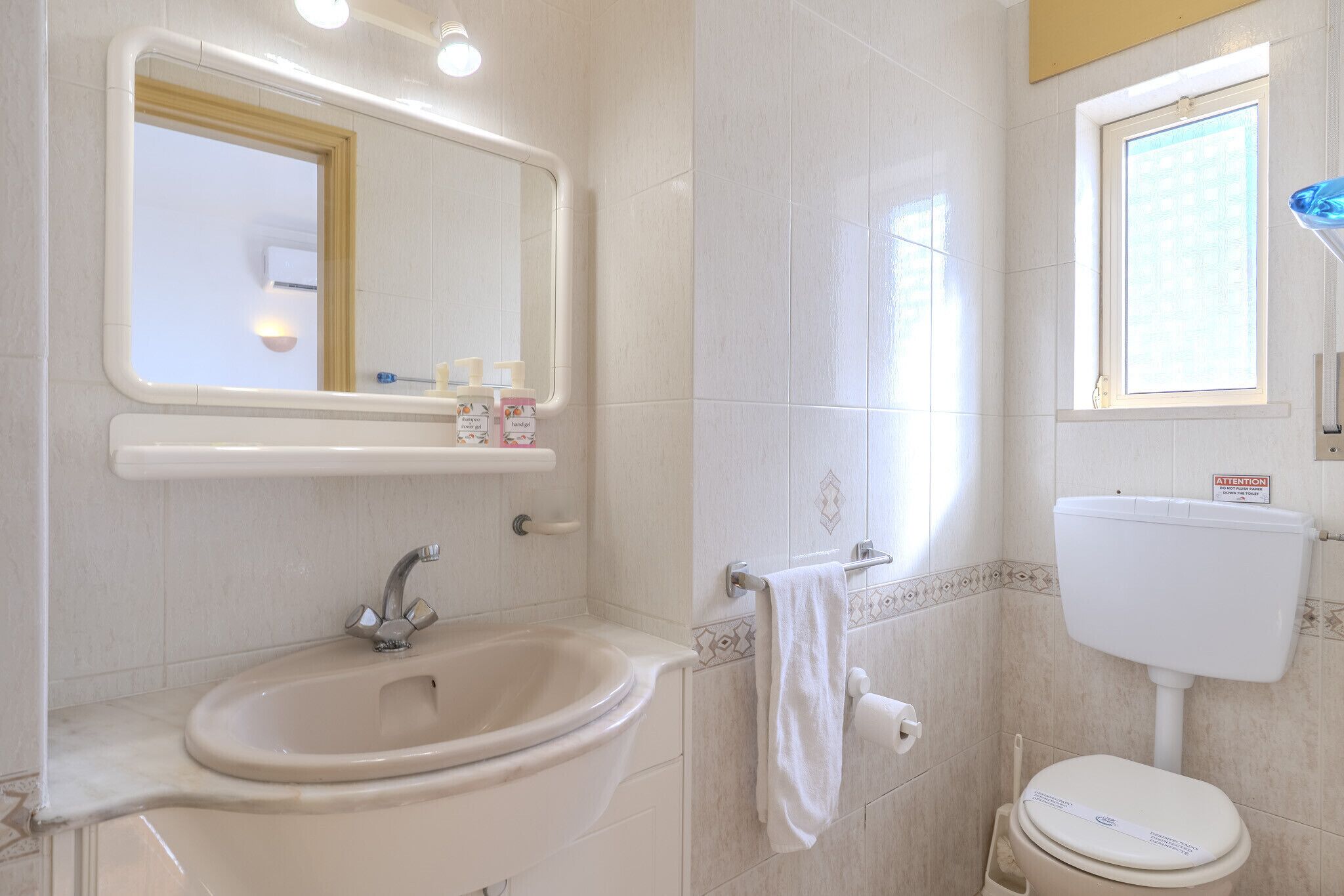 A bathroom with a sink, mirror, toilet, and window.