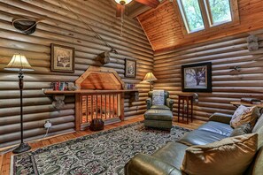 Interior de una cabaña de madera con chimenea, sofá de cuero y alfombra estampada.