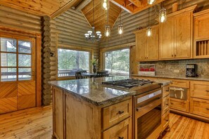 A log cabin interior with a kitchen island, wooden cabinets, a dining area, and large windows. - Lakefront Log Elegance: True Cabin with Hot Tub and Sauna Amidst Mountain Views (Gilmer County)