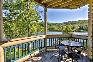 Un espace extérieur abrité, doté d’une table et de chaises, qui offre une vue sur un lac et des collines boisées.