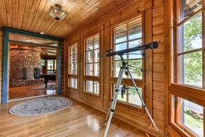 Un interior de madera con ventanas amplias, una chimenea de piedra y un telescopio.