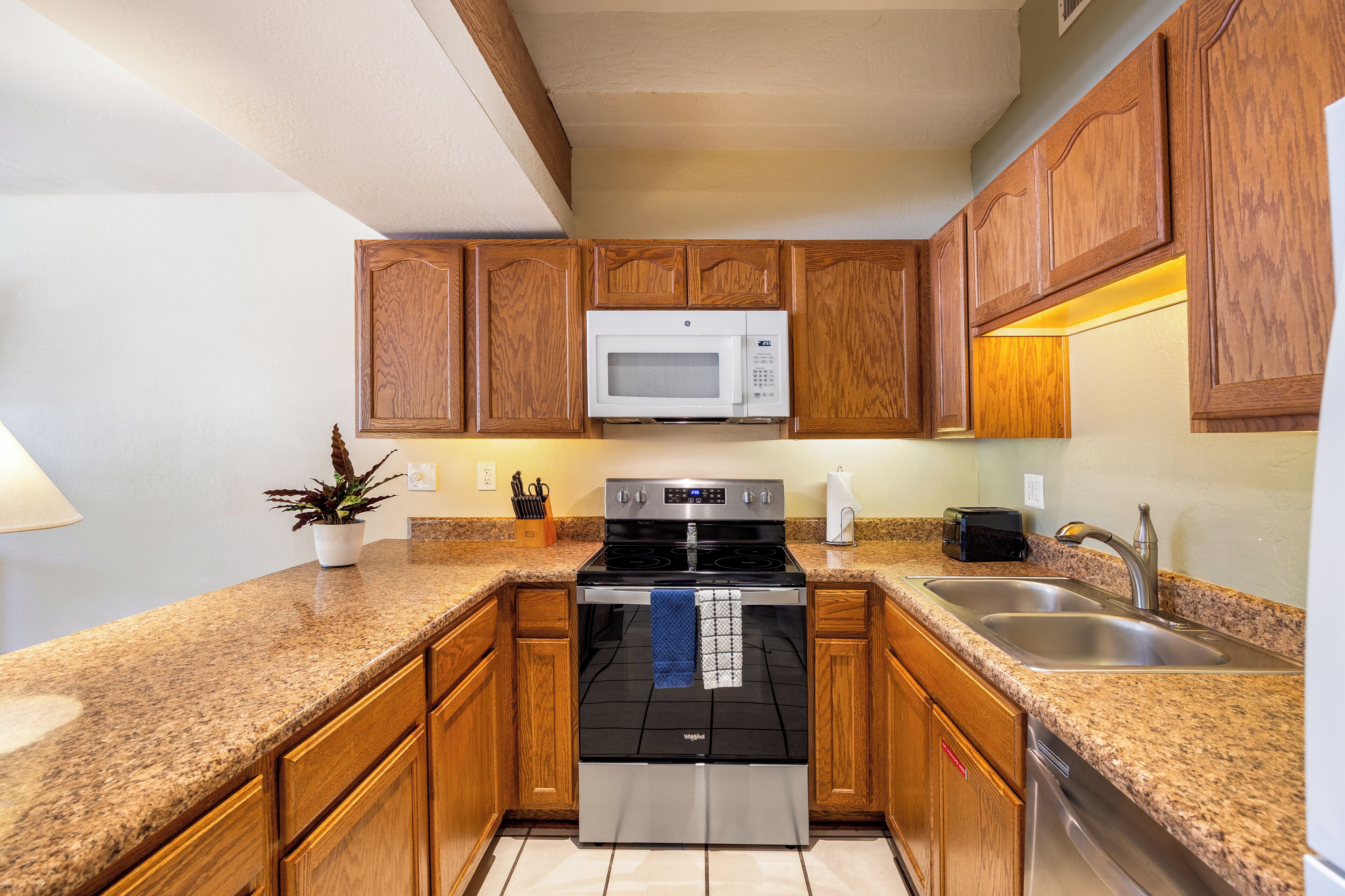A kitchen with wooden cabinets, a stainless steel stove, a microwave, and a sink.