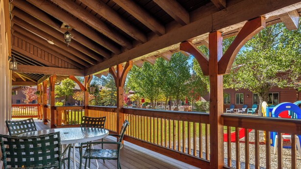 A covered outdoor area with a wooden deck, a table with chairs, and a playground in the background. - Juniper-Boardwalk by Roundhouse Resort and Spa (Pinetop Country Club)