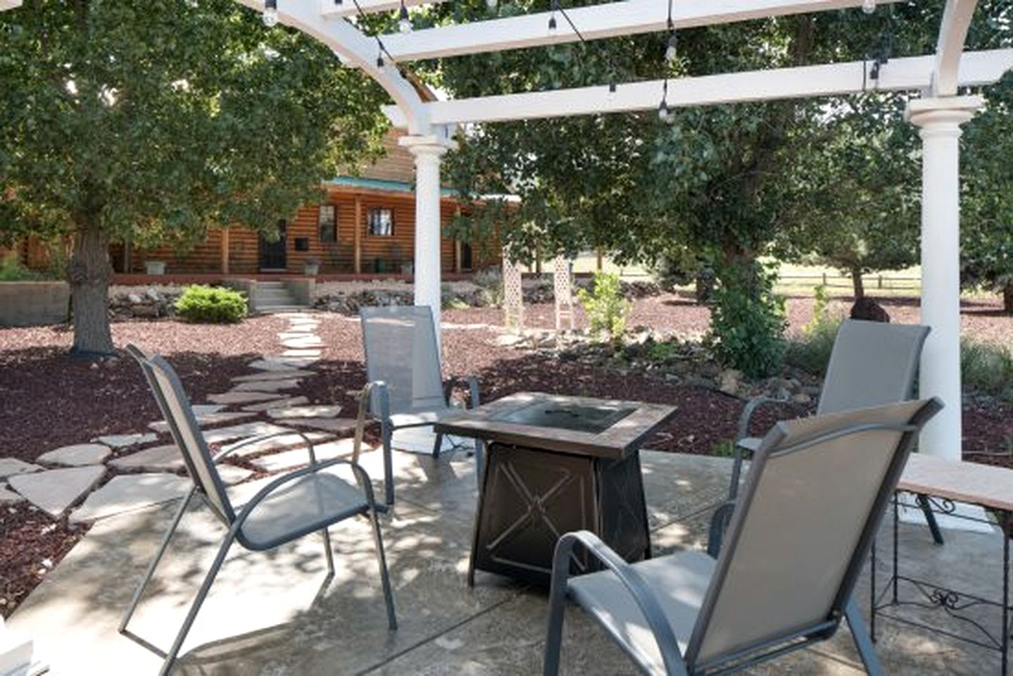 An outdoor patio with a pergola, stone pathway, and seating area with chairs and a table.