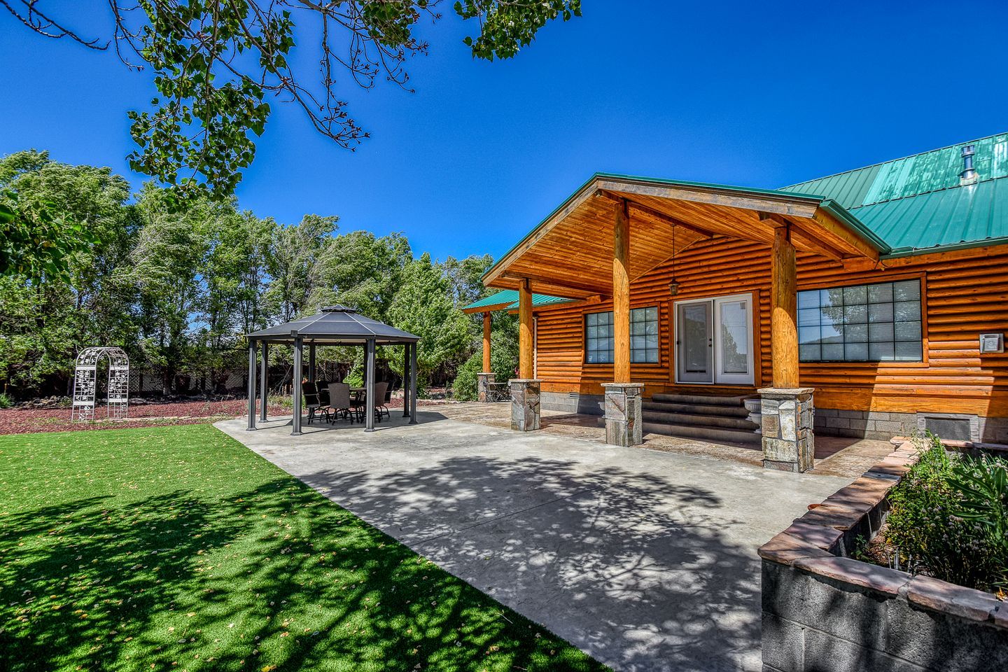A wooden cabin with a covered patio, a gazebo, and a stone retaining wall.