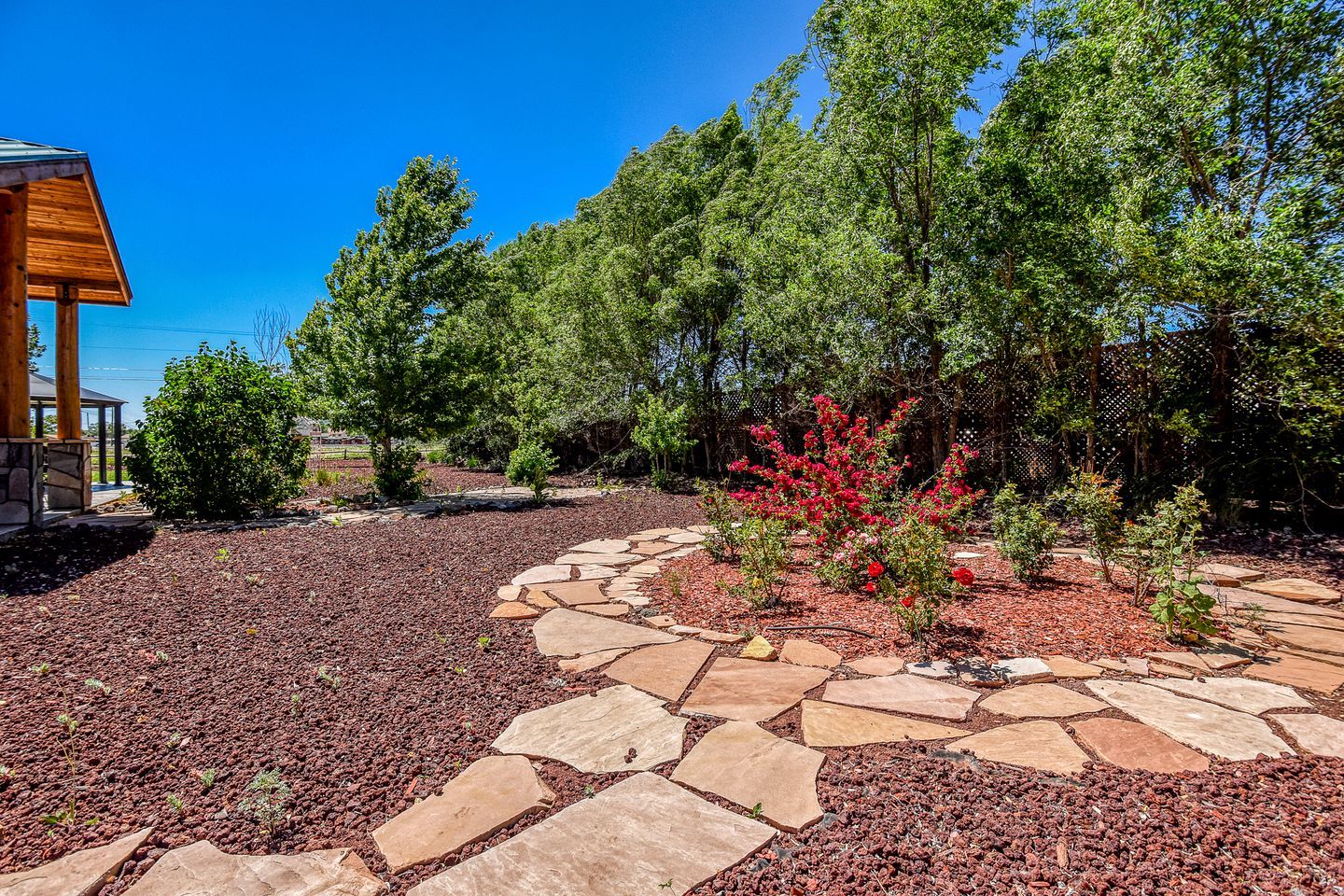 A landscaped garden with a stone pathway, trees, and a wooden structure.