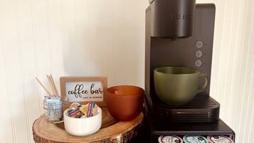 A coffee maker with a cup holder, a bowl of snacks, and a coffee bar sign.