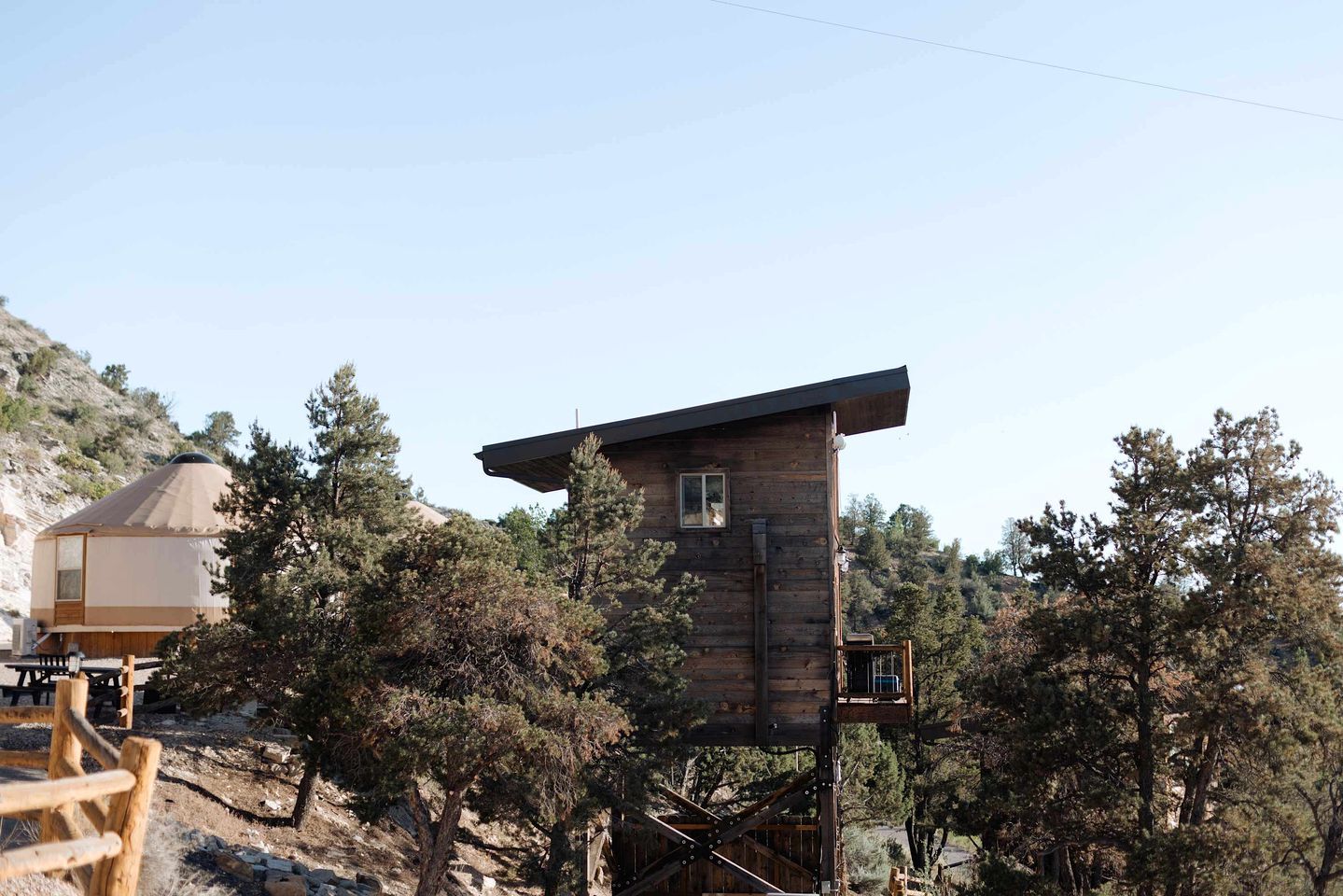 Une cabane en bois dotée d’un balcon, entourée d’arbres et surplombant un ciel dégagé.
