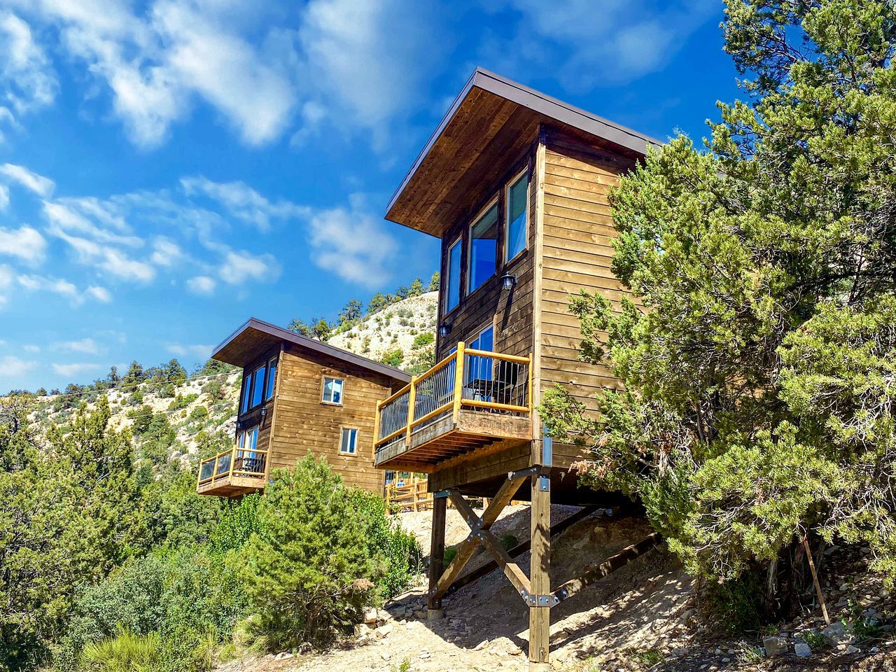 A wooden cabin with a balcony, situated on a hillside with trees.