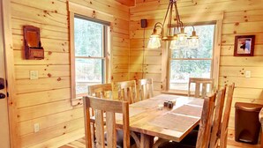 Interior de una cabaña de madera con una mesa de comedor, sillas y una araña.
