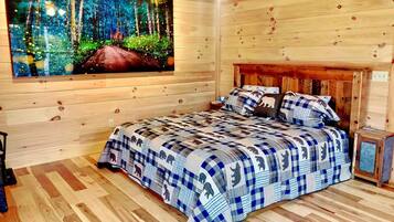 A wooden cabin bedroom with a bed, a painting of a forest, and a small cabinet.