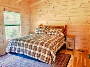 Ein Schlafzimmer einer Holzhütte mit einem Bett, einem Nachttisch und einem Fenster.