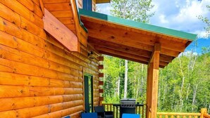Una cabaña de troncos con terraza, asientos exteriores y una parrilla.