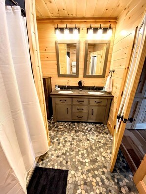 Een houten badkamer in een chalet met twee wastafels, een spiegel en een douchegordijn.