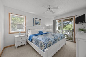 Ein Schlafzimmer mit Bett, Nachttischen, Deckenventilator, großem Fenster und einer Schiebeglastür zum Balkon.