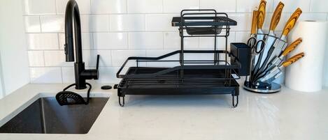 A kitchen with a sink, a black metal drying rack, and a knife block with wooden handles.