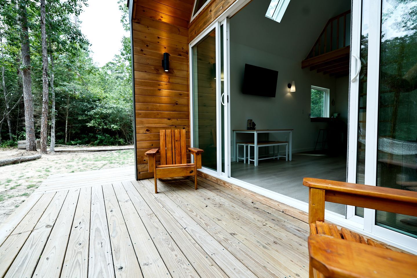 A wooden deck with a chair, a table, and a TV in a modern cabin with glass doors.