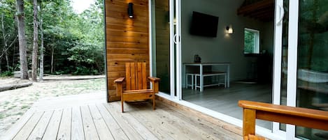 A wooden deck with a chair, a table, and a TV in a modern cabin with glass doors.