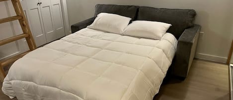 Una cama con edredón blanco, cabecera oscura y escalera de madera.